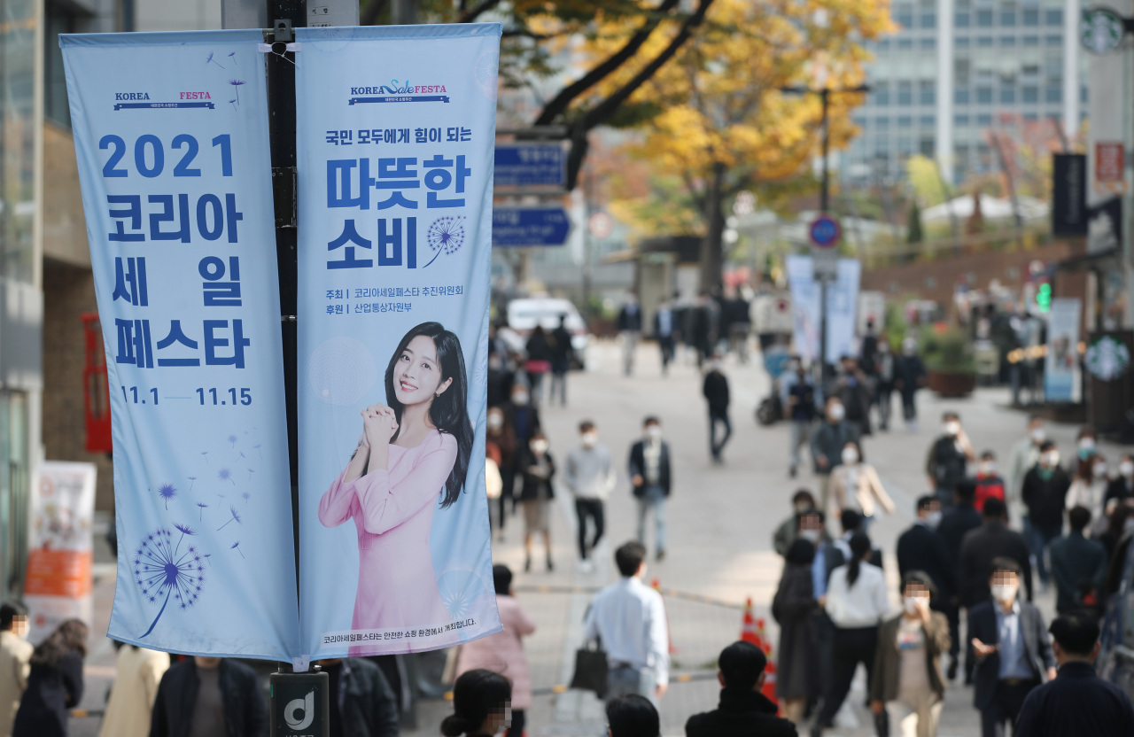 People walk past signs promoting the 2021 Korea Sale FESTA in the shopping district of Myeongdong in Seoul last Monday, the first day of the 15-day event to attract foreign tourists and boost domestic consumption. (Yonhap)