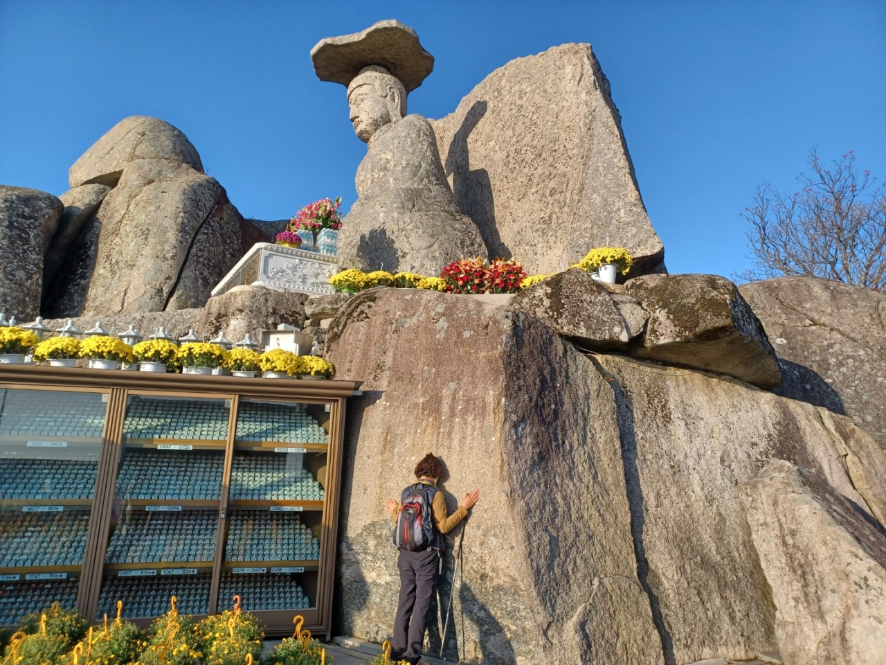 A woman prays next to a rock under the Buddha statue after placing her coin on the rock’s surface. (Lee Si-jin/The Korea Herald)
