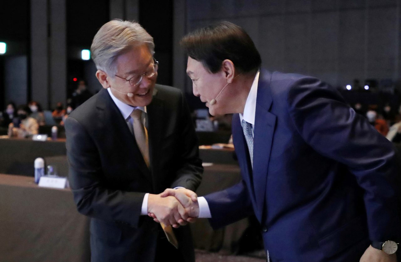 Democratic Party of Korea`s presidential nominee Lee Jae-myung (left) exchanges greeting Monday with Yoon Seok-youl (right), presidential nominee of the main opposition People Power Party, as they both attend a forum held in Seoul. (Joint Press Corps)