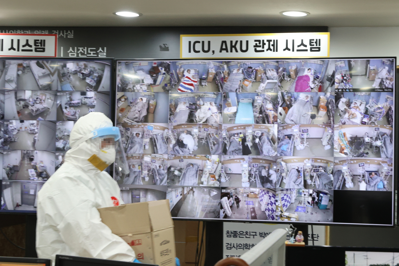 A patient transfer official passes in front of the video of the hospital room control system in the situation room of Bagae Hospital in Pyeongtaek, a hospital dedicated to COVID-19 on Tuesday. (Yonhap)
