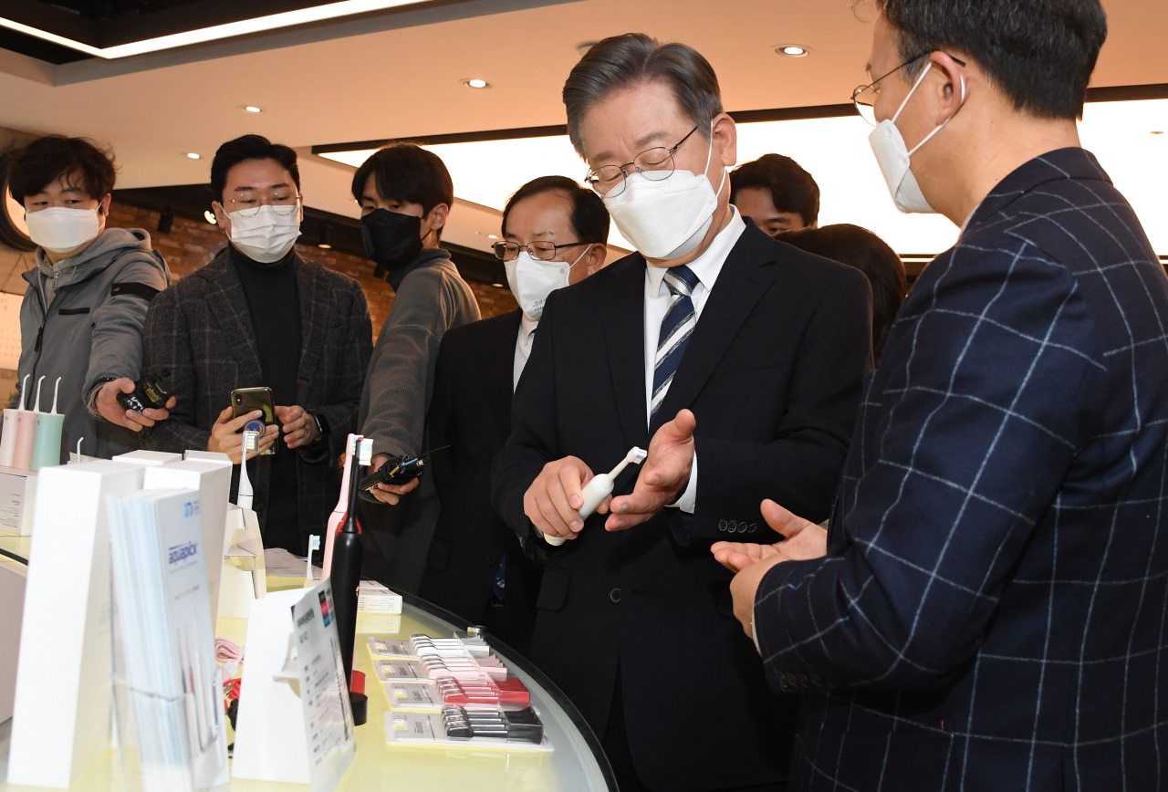 Lee Jae-myung (2nd from R), the presidential nominee of the Democratic Party, takes a look at products made by small and medium-sized businesses at an industrial complex in southwestern Seoul on Wednesday. (Yonhap)