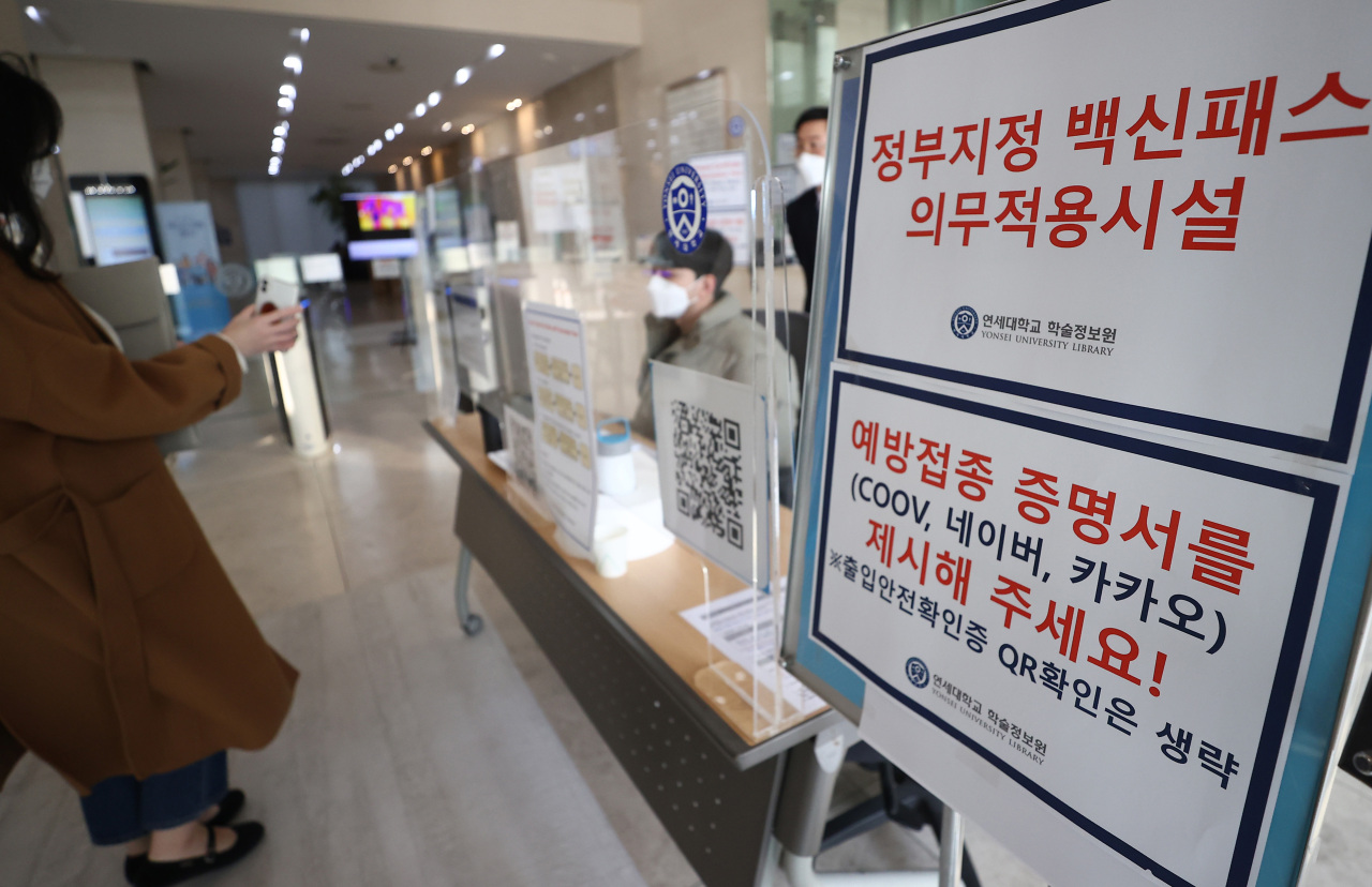 A student shows a vaccination pass in front of a library at Yonsei University in Seoul on Sunday. (Yonhap)