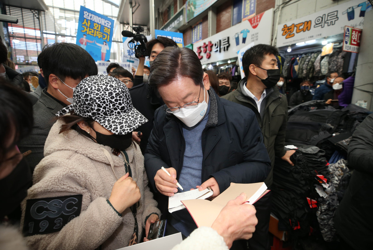 Lee Jae-myung, the presidential candidate of the ruling Democratic Party of Korea, gives his autograph to a supporter while canvassing in a traditional market in Pohang, North Gyeongsang Province, Monday. (Yonhap)