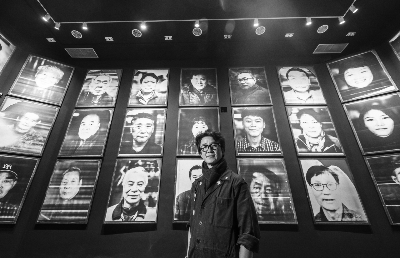 MJ Kim stands in front of his portrait photographs of everyday people. (MJ Kim)