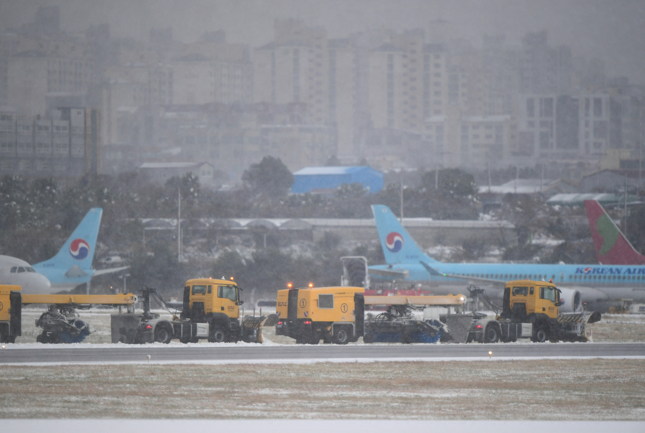 Workers clear snow on runway at Jeju International Airport on Sunday (Yonhap)