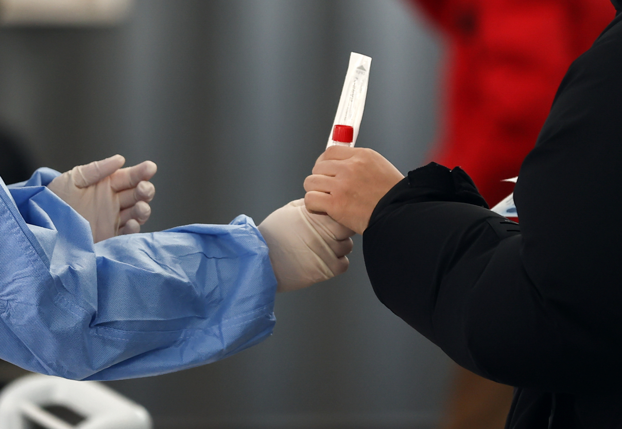 This file photo taken Tuesday shows a medical worker handing a COVID-19 testing kit to a person at a COVID-19 testing center in central Seoul. (Yonhap)