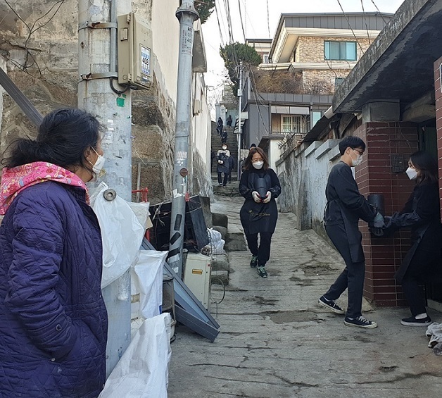 Yang Jae-sook (left) watches as volunteers deliver coal briquettes to her house at Samseon-dong in Seongbuk-gu, northern Seoul, on Dec. 22. (Choi Jae-hee / The Korea Herald)