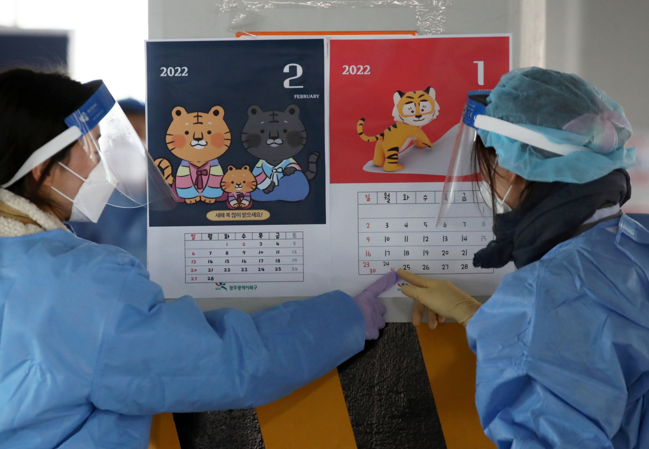 Medical workers talk to each other while pointing to calendars for 2022, the Year of the Tiger in the Chinese zodiac, as they prepare to administer coronavirus tests at a screening clinic in the southwestern city of Gwangju last Thursday. (Yonhap)