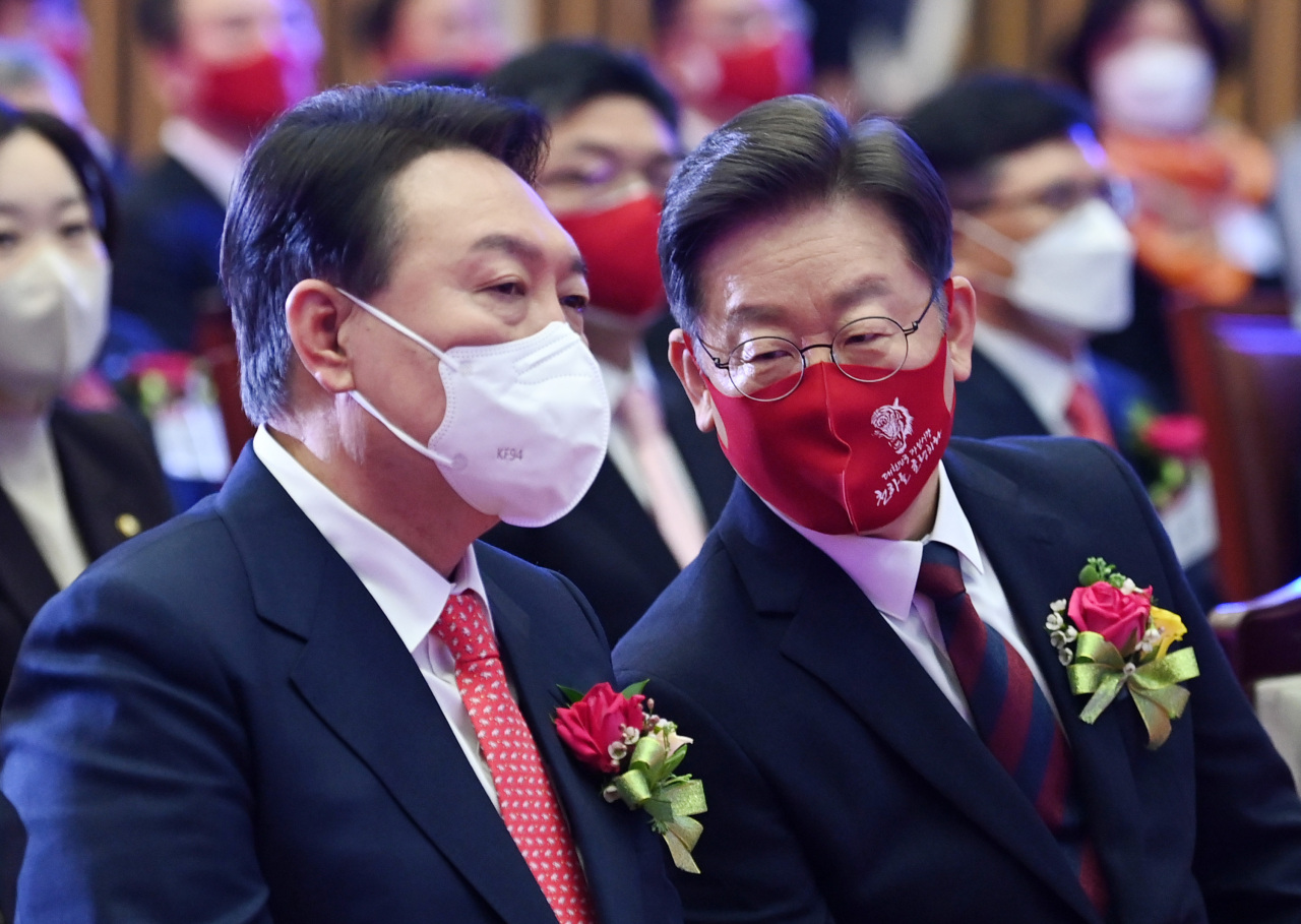 Yoon Suk-yeol (left), presidential nominee of the main opposition People Power Party, talks with his rival Lee Jae-myung from the ruling Democratic Party of Korea during an event held Monday. (Joint Press Corps)