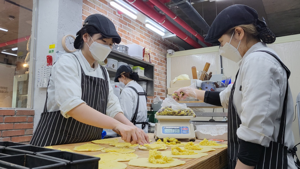Pastry chefs add filling to dough in the Yangsuri Bread Factory’s kitchen. (Kim Hae-yeon/The Korea Herald)