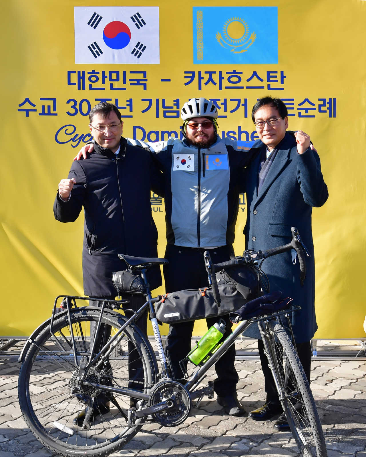 Kazakh Ambassador to Korea Bakyt Dyussenbayev (left), Kazakhstani cyclist Damir Kusheyev (center) and Seoul Cyber University Vice President Park Hyun-seok pose for a picture at Seoul Cyber University, celebrating Kusheyev’s completion of his cycling trip. (Seoul Cyber University)