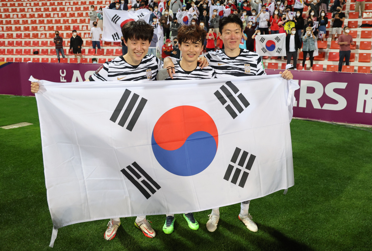 South Korean players Hwang In-beom, Kim Min-jae and Paik Seung-ho (L to R) celebrate with their national flag, Taegeukgi, after the team clinched a berth for the 2022 FIFA World Cup with a 2-0 victory over Syria in Group A match during the final Asian qualifying round at Rashid Stadium in Dubai on Tuesday. (Yonhap)