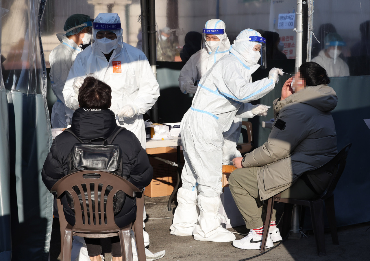 Medical workers carry out rapid antigen tests at a COVID-19 testing station in Seoul on Friday, when the country reported 27,443 new cases. (Yonhap)