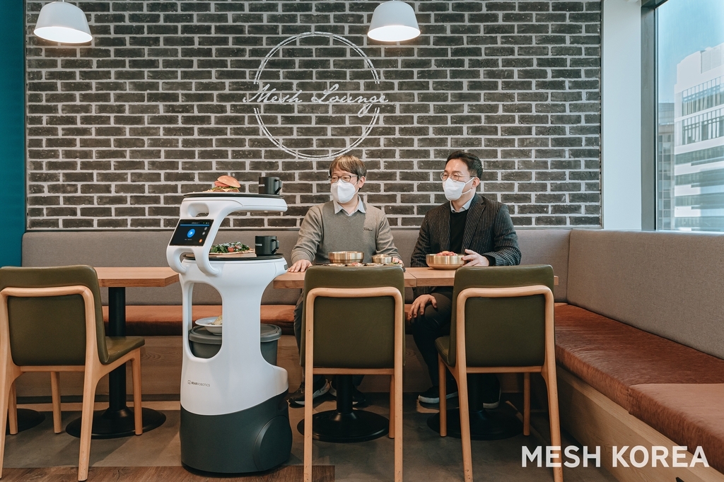 Mesh Korea Chief Technology Officer Kim Myeong-hwan (left) and Bear Robotics Korea CEO Kim Jun-su are served by a robot prototype planned for high-rise building delivery services at a demonstration session held at Mesh lounge in Seoul in January. (Mesh Korea)