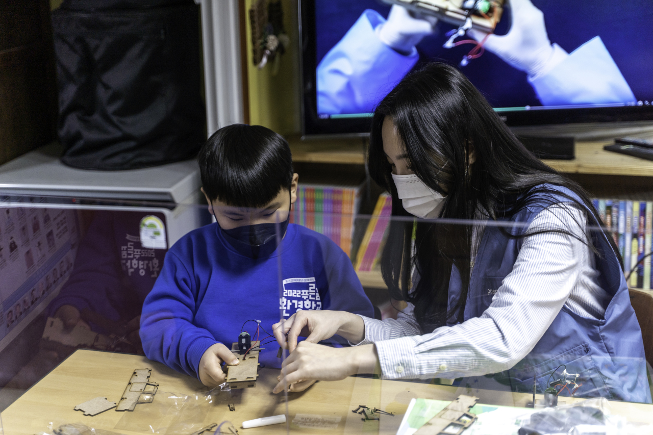 A Posco Chemical official assembles a miniature electric vehicle with a student at a culture center in Pohang, North Gyeongsang Province. (Posco Chemical)