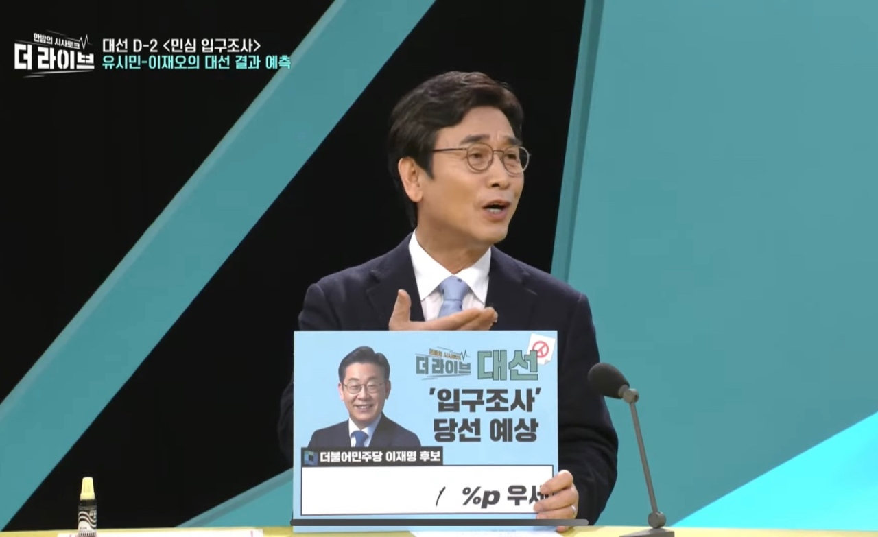 Rhyu Si-min, a liberal commentator and former chairman of the Roh Moo-hyun Foundation, holds up card to predict that the ruling party’s presidential candidate Lee Jae-myung will beat his conservative rival Yoon Suk-yeol by 1 percentage point, in a KBS TV program on Monday. (Screen captured from KBS The Live YouTube channel)