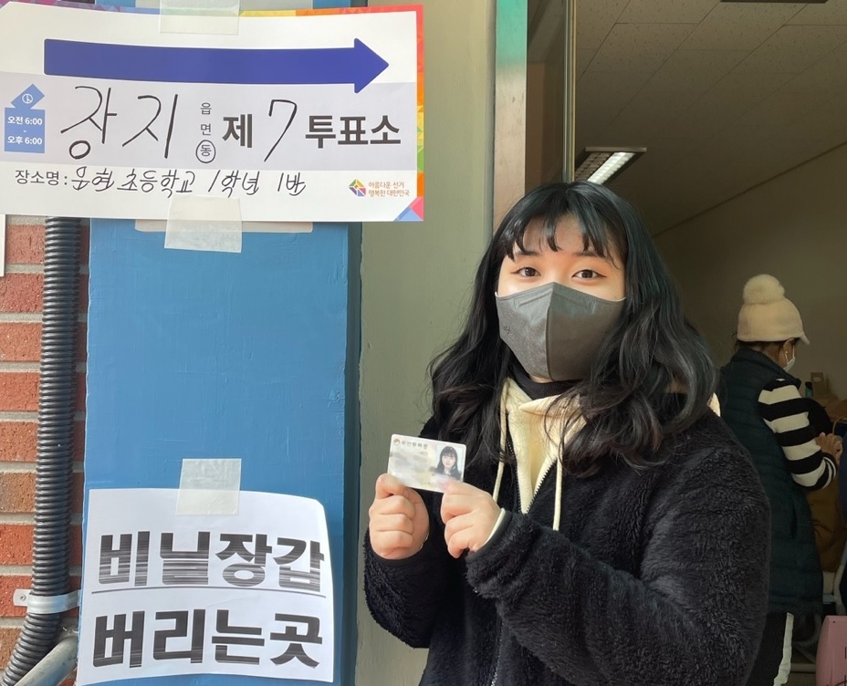 Kim Ji-su, 18, holds up her ID card and poses in front of a polling station sign in Songpa-gu, Seoul on Wednesday. (On the courtesy of Kim)