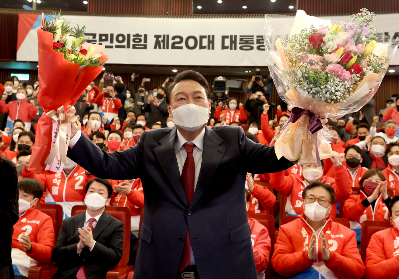 President-elect Yoon Suk-yeol poses for photos after receiving flowers in his party's election situation room at the National Assembly in Seoul on Thursday. (Yonhap)