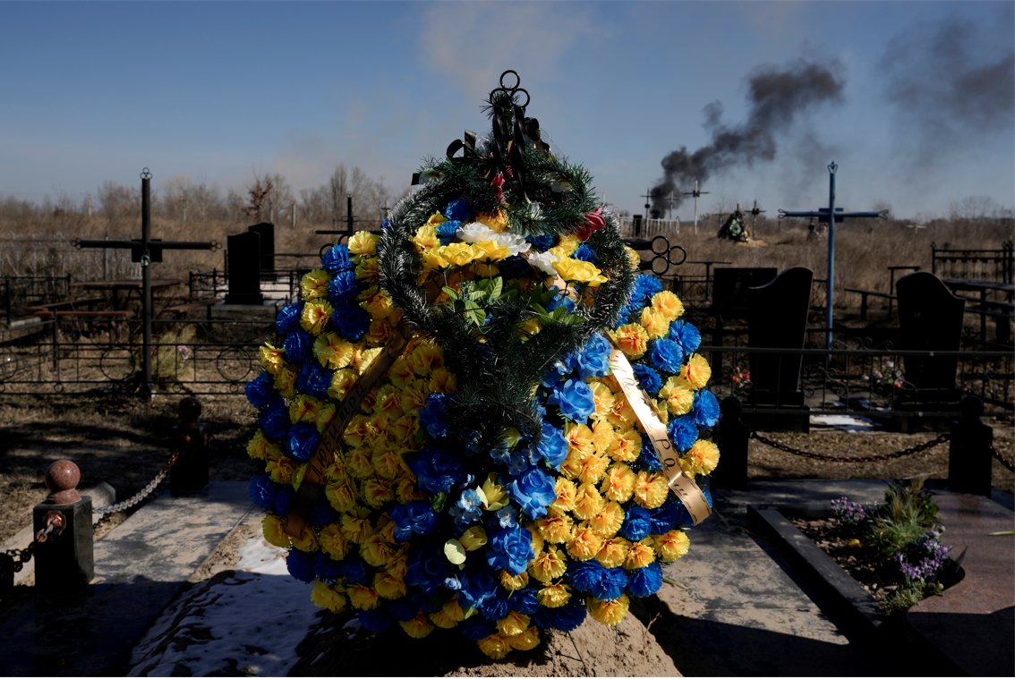 Smoke from shelling rises as a wreath of flowers is placed at a cemetery in Vasylkiv south west of Kyiv, Ukraine on Saturday. (AP Photo/Vadim Ghirda)