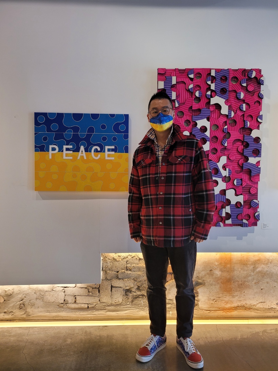 Heo Wook stands next to his painting “PEACE in Ukraine” wearing a face mask designed with the image at Jeongdong 1928 Gallery in Seoul. (Park Yuna/The Korea Herald)