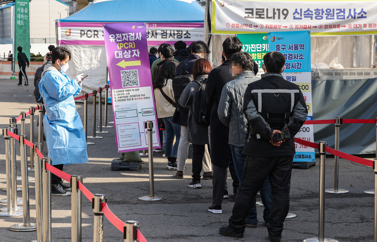 People stand in line to take coronavirus tests at a makeshift testing station in front of Seoul Station on Tuesday. (Yonhap)