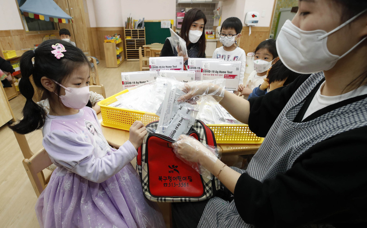 A worker at a Gwangju child care center hands a set of COVID-19 at-home testing kits to a child on March 2. (Yonhap)
