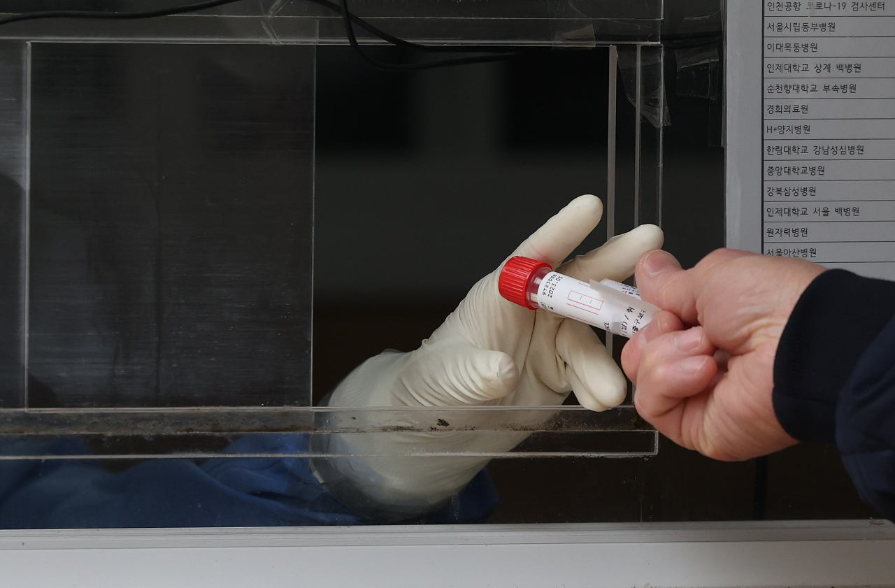 A person gives a COVID-19 test sample to medical staff behind a screen at a testing booth near Seoul Station on Wednesday. (Yonhap)