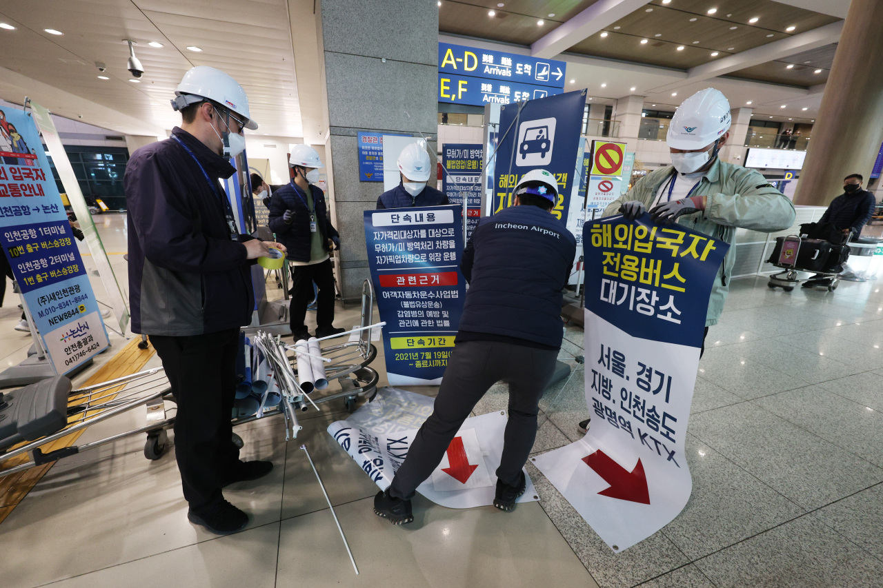 Airport officials remove signage indicating a waiting area for buses exclusively for overseas inbound travelers, designed to separate them from others for prevention of potential exposure to COVID-19, in the arrivals hall of Terminal 1 of Incheon Airport on April 1. (Yonhap)