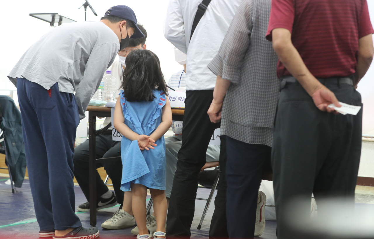 A child looks on as her father prepares to vote at a polling booth in Busan during Wednesday’s local elections. (Yonhap)