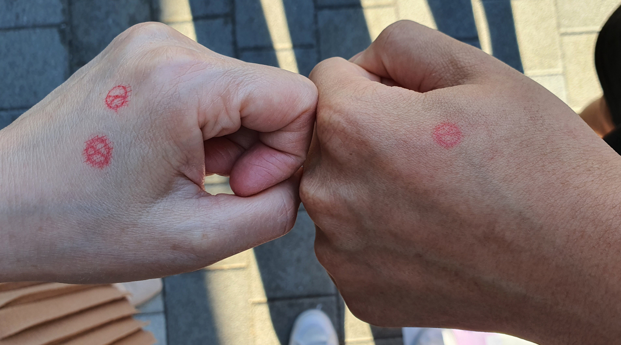 Two voters show election stamps on their hands outside a polling station in Seoul’s Seocho district on Wednesday. The display of election ink smudged on a hand is the most popular type of “voting proof shots” which inundate social media whenever there is an election in South Korea.(Yonhap)