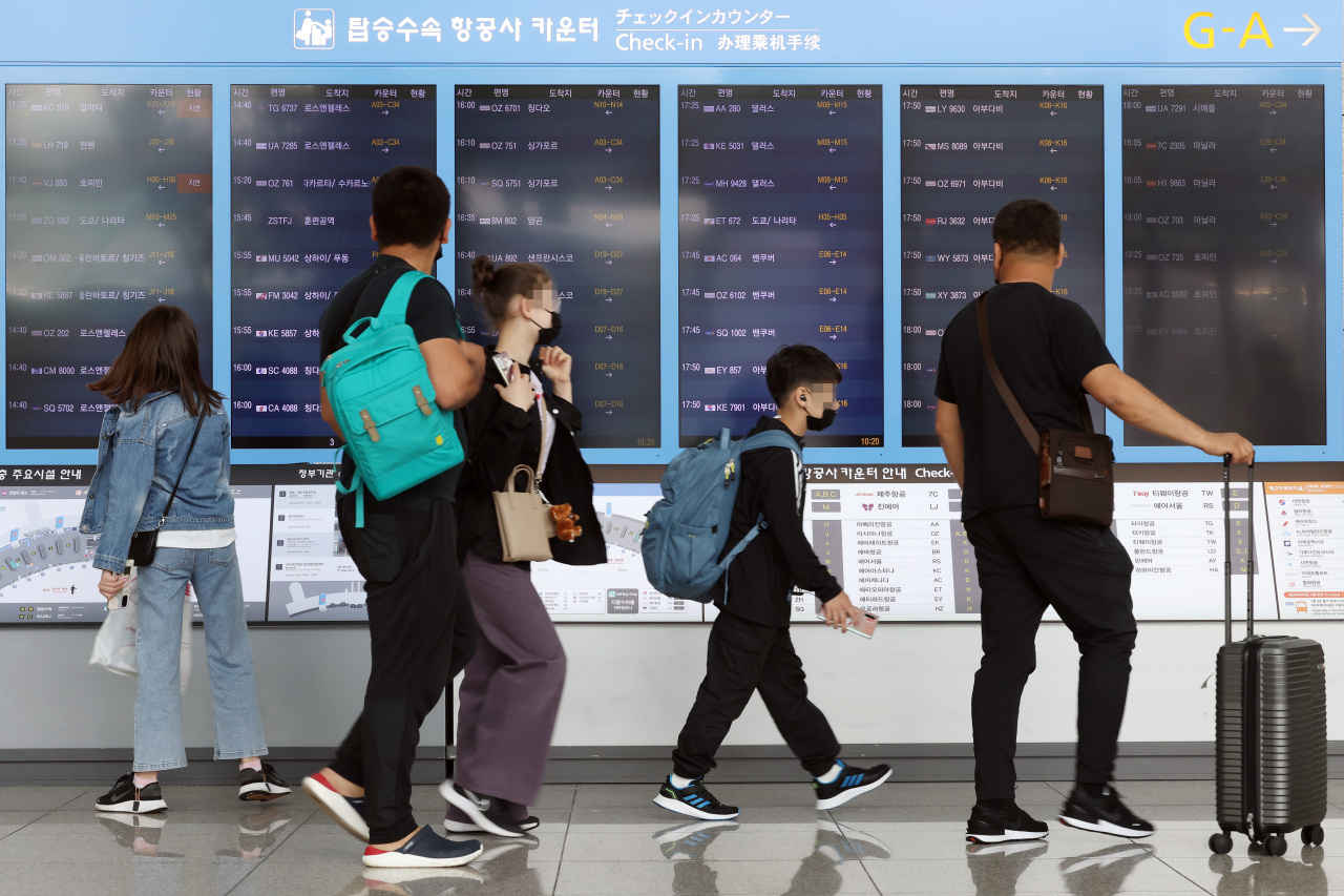Passengers walk past an electronic board showing flight schedules at Incheon International Airport in Incheon, Friday. (Yonhap)