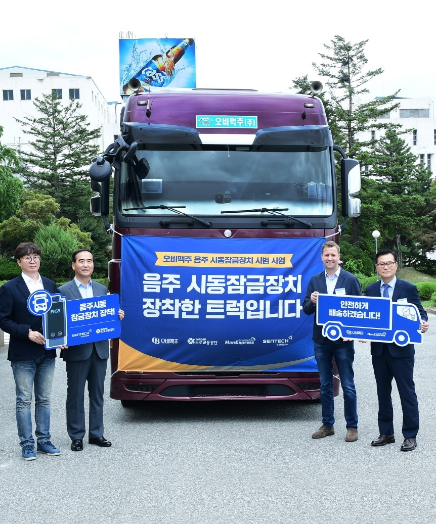 From left: Sentech Korea CEO Yoo Do-joon, KoROAD Chairman Lee Joo-min, OB CEO Ben Verhaert and Han Express director Yoon Young-chae pose in front of a truck equipped with an ignition interlock device at OB’s factory in Icheon, Gyeonggi Province, on June 28. (Oriental Brewery)