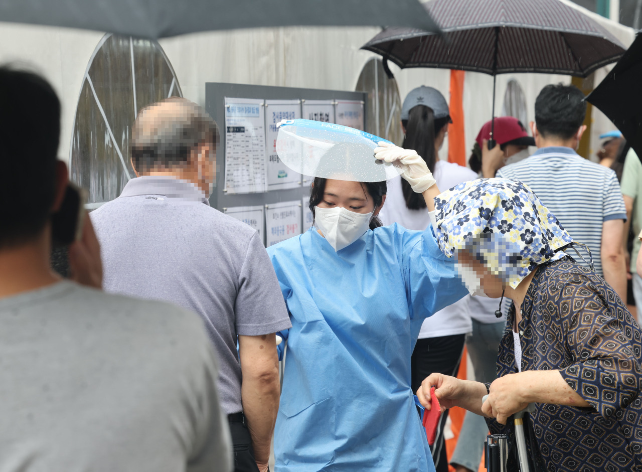 People wait in rain at a local COVID-19 testing station in Gangnam-gu, Seoul. (Yonhap)