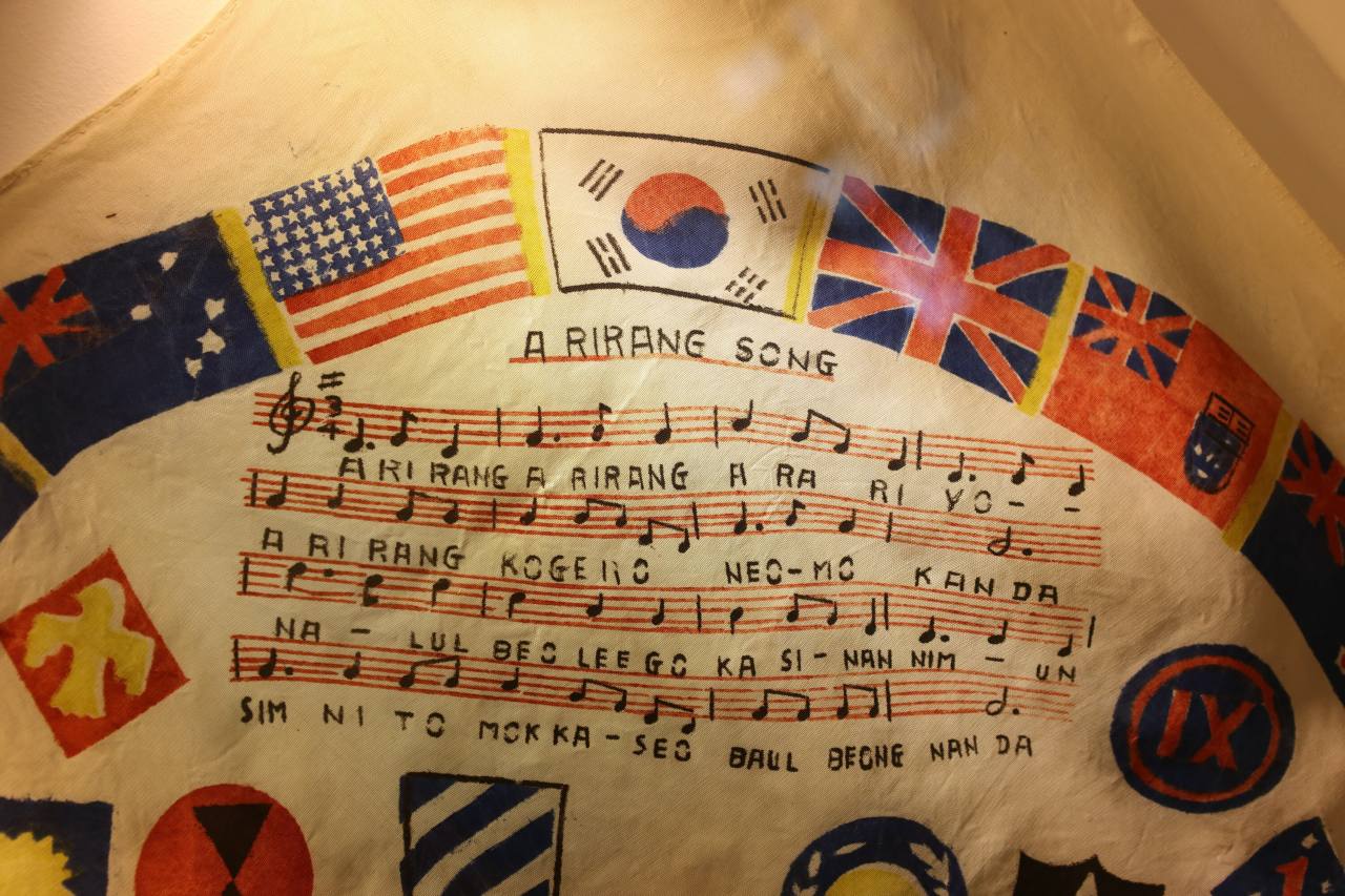 1951년 스카프는 한국전쟁에 참전한 유엔군의 깃발이 있는 아리랑 악보를 보여줍니다.  일부 외국 음악가들은 한국에서 귀국하여 아리랑 선율을 녹음했습니다.  사진 © 강형원