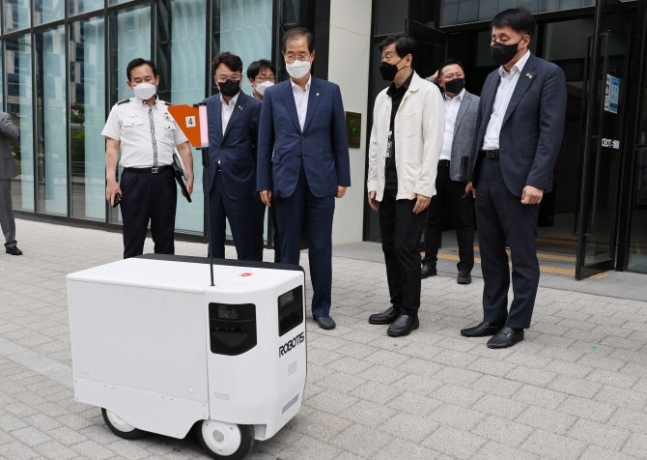 Prime Minister Han Duck-soo (center) visits the headquarters of a local robotics company, called Robtis, in Seoul in June. The government mulls regulatory easing to speed up the market debut of sidewalk robots for delivery. (Yonhap)