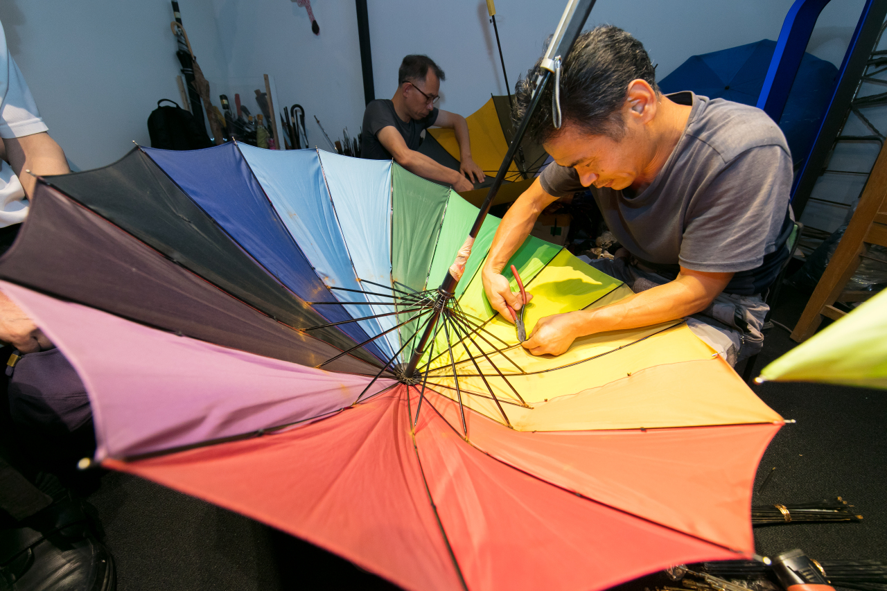 A staff member demonstrates how to fix umbrellas during a workshop held at the National Folk Museum of Korea’s outdoor exhibition ”Street of Memories.” (NFMK)