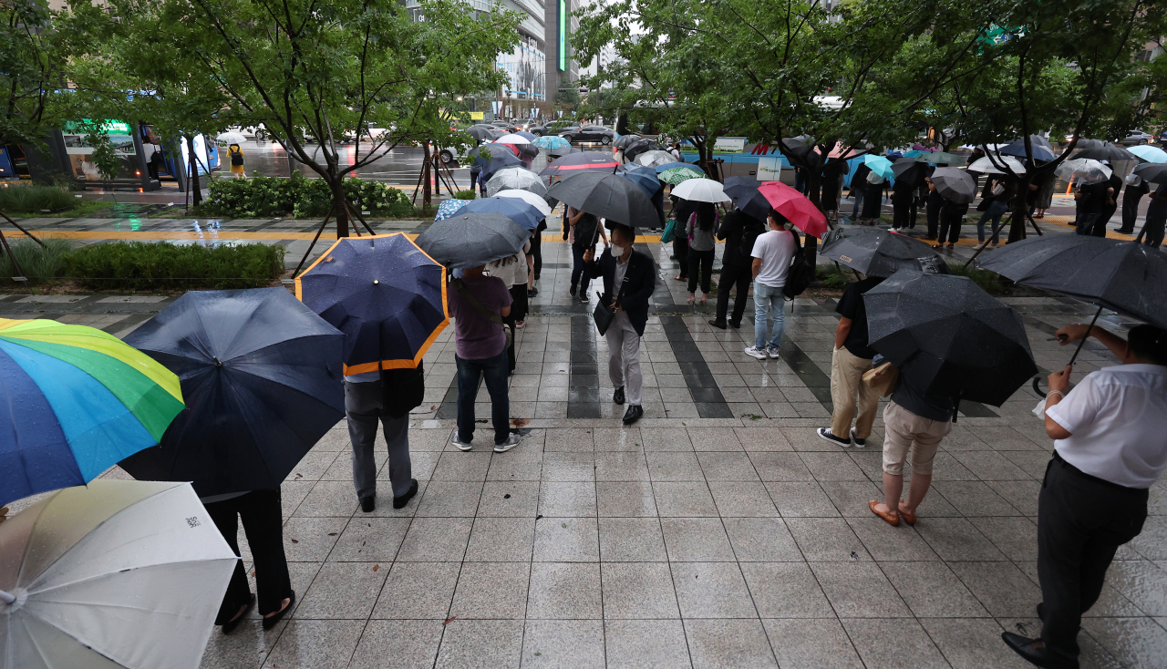 People waiting in line for city buses in Jongno-gu, central Seoul, amid heavy rain on Tuesday afternoon. (Yonhap)