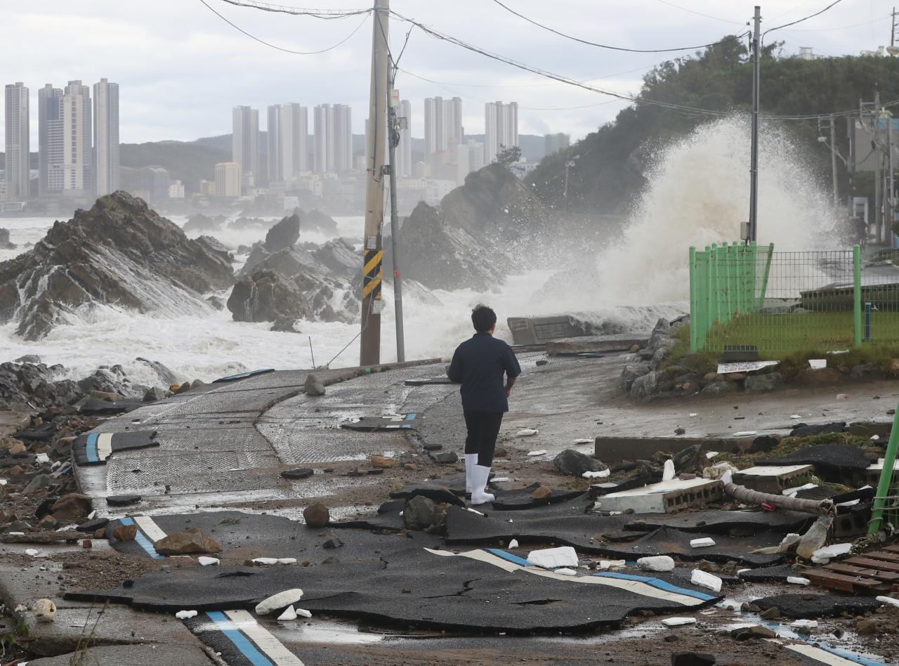 A resident walks down a collapsed road alongside the coast of Ulsan on Tuesday morning after Typhoon Hinnamnor moved out of South Korea, passing through the city. (Yonhap)
