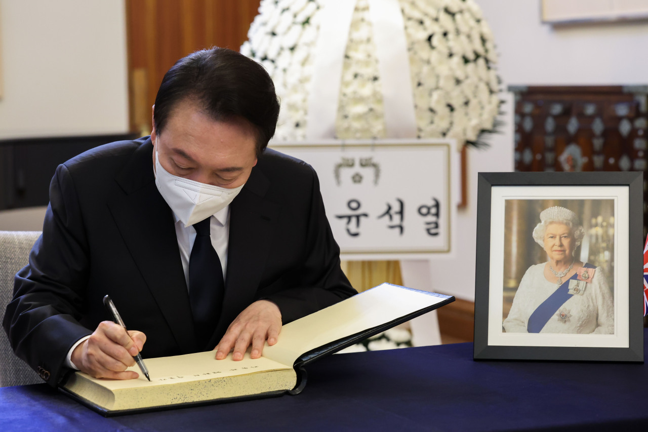 South Korean President Yoon Suk-yeol writes in the guest book after paying respects to Britain's Queen Elizabeth II, at the altar prepared at the British Embassy in Seoul on Friday. (Yonhap)
