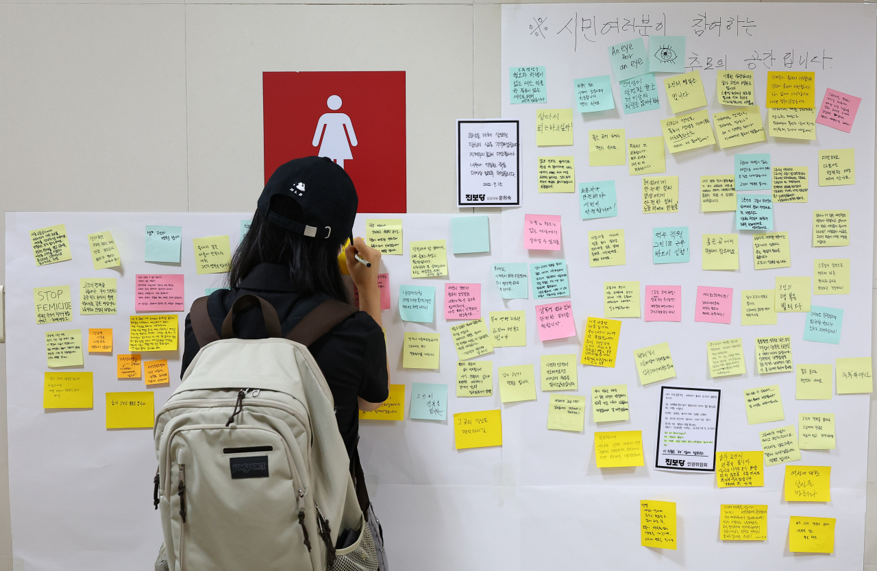 A passerby on Friday writes a message of condolences for a victim murdered Wednesday by a stalking perpetrator. Many mourners visited the restroom at Sindang Station in Seoul, where the murder occured, to lament the injustice. (Yonhap)