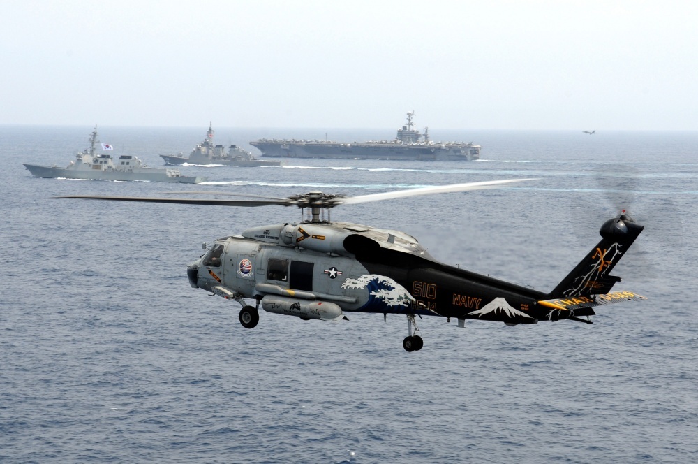 In this file photo, an SH-60F Seahawk helicopter, assigned to the Chargers of Helicopter Anti-Submarine Squadron (HS) 14, is airborne while the aircraft carrier USS George Washington (CVN 73), the Japan Maritime Self-Defense Force destroyer JS Kirishima (DD 174), and the Republic of Korea navy destroyer ROKS Sejong the Great (DDG 991) participate a trilateral event, June 22, 2012. (US Department of Defense)