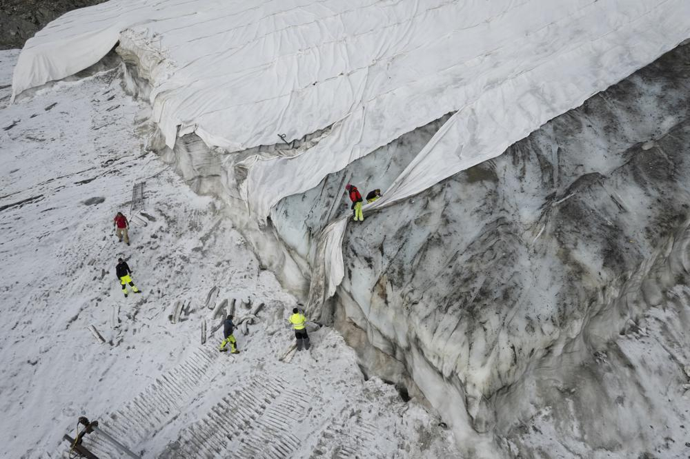 People work on a tarpaulin which cover the ice of the Corvatsch glacier, near Samedan, Switzerland, on Sept. 5, Glaciologists have stopped their program to measure the glacier. The decision has already been taken in 2019 and the hot summer of 2022 has led to 