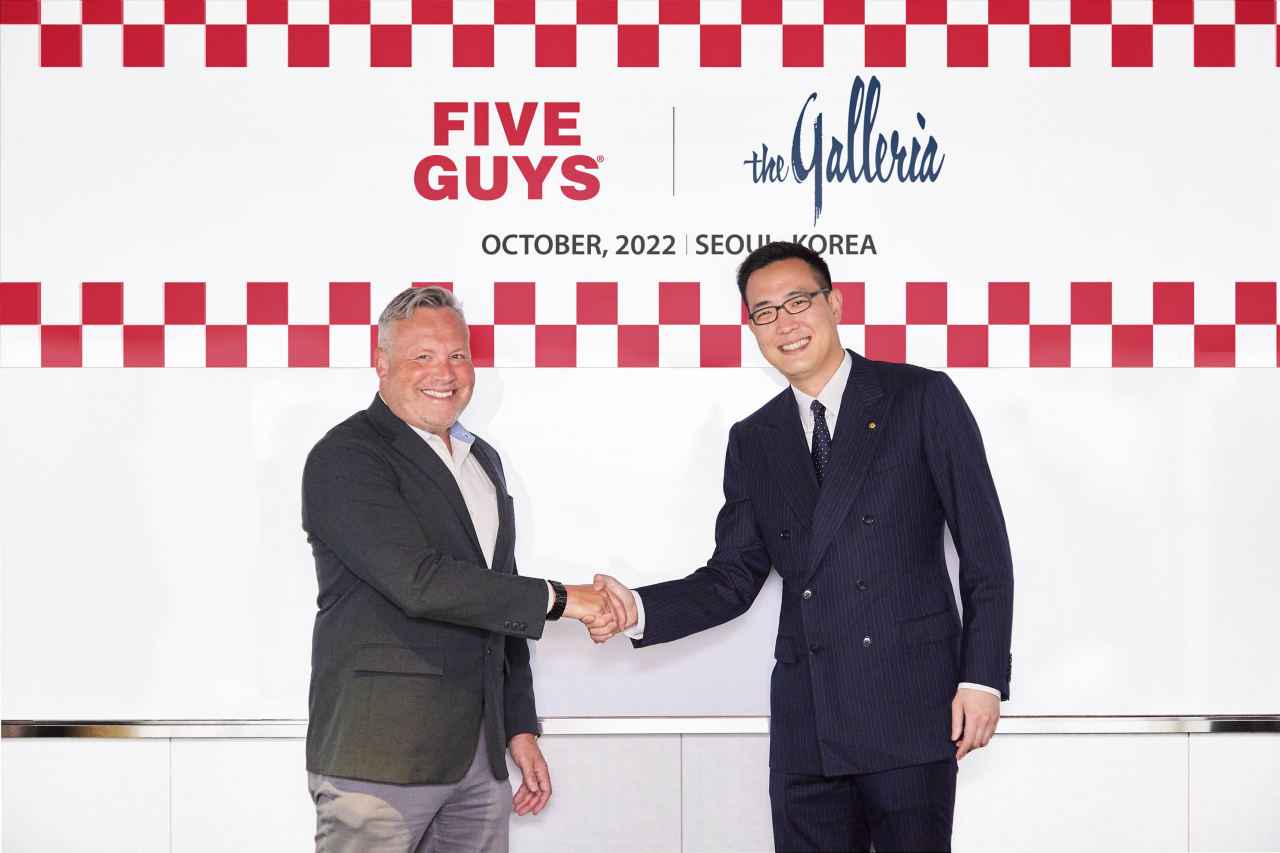 Kim Dong-sun (right), head of strategic management at Hanwha Galleria and director at Hanwha Hotel and Resorts, shakes hands with William Fisher, director of international expansion at Five Guys Enterprise, for a photo at The Plaza Seoul in Jung-gu central Seoul on Wednesday. (Hanwha Galleria)