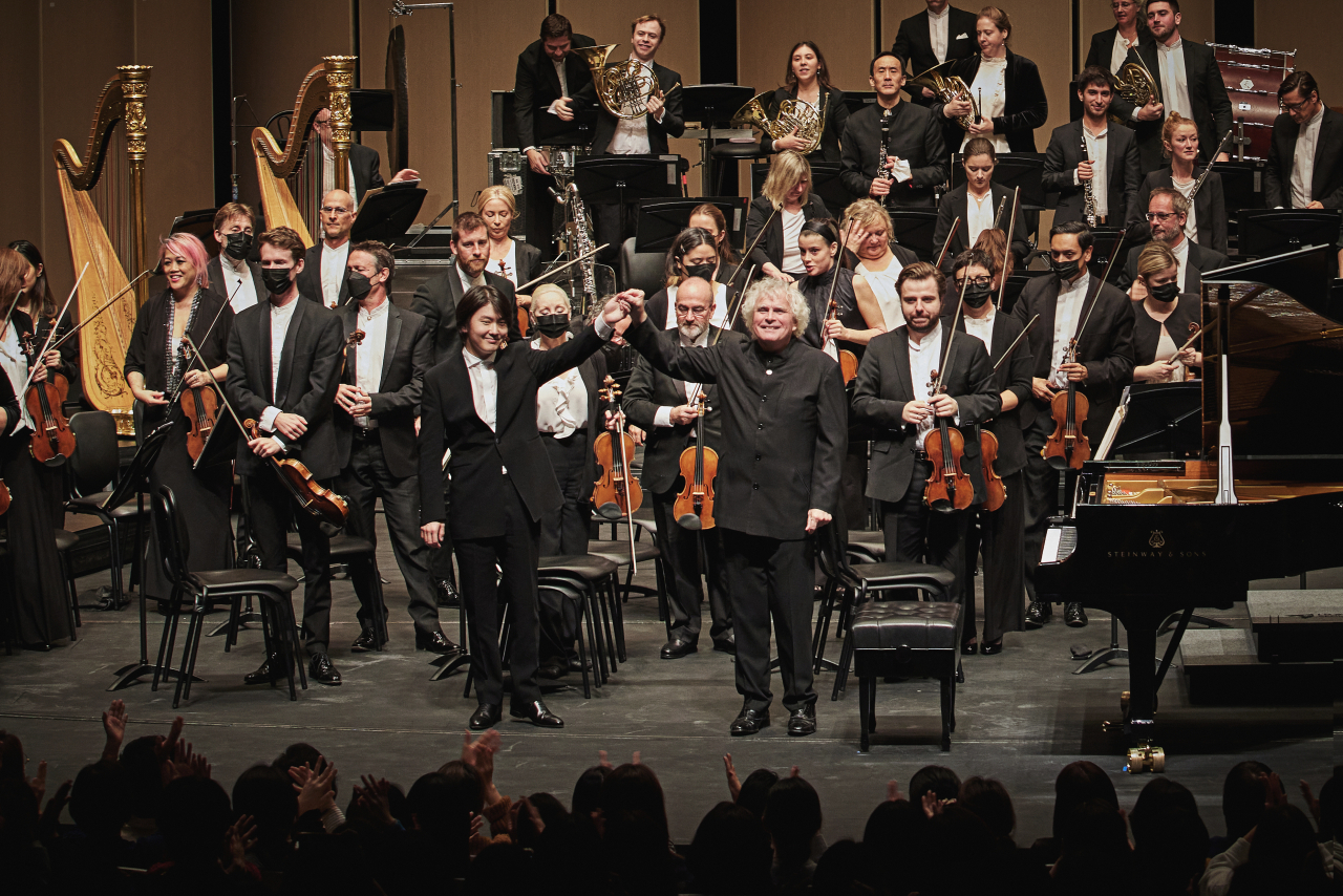 Korean pianist Cho Seong-jin (front, left) and Sir Simon Rattle, the music director of the London Symphony Orchestra, greet the audience with the London Symphony Orchestra on Thursday at LG Arts Center in Magok, Seoul. (LG Art Center)