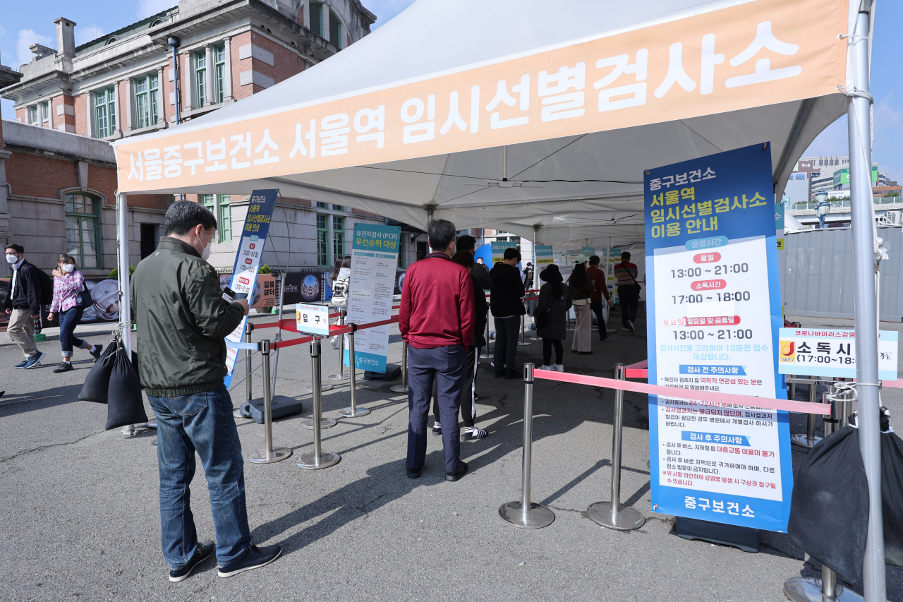 People stand in line to undertake COVID-19 tests at a makeshift testing station in Seoul on Sunday. South Korea reported 26,256 new infections on the day, up by 4,800 cases from the previous week, the Korea Disease Control and Prevention Agency said. (Yonhap)