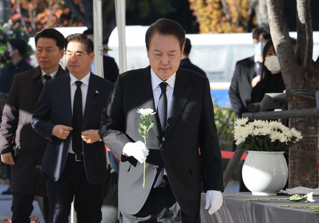 President Yoon Suk-yeol carries a chrysanthemum to a mourning altar for victims of the Halloween crowd crush in front of City Hall in Seoul on Friday. (Yonhap)