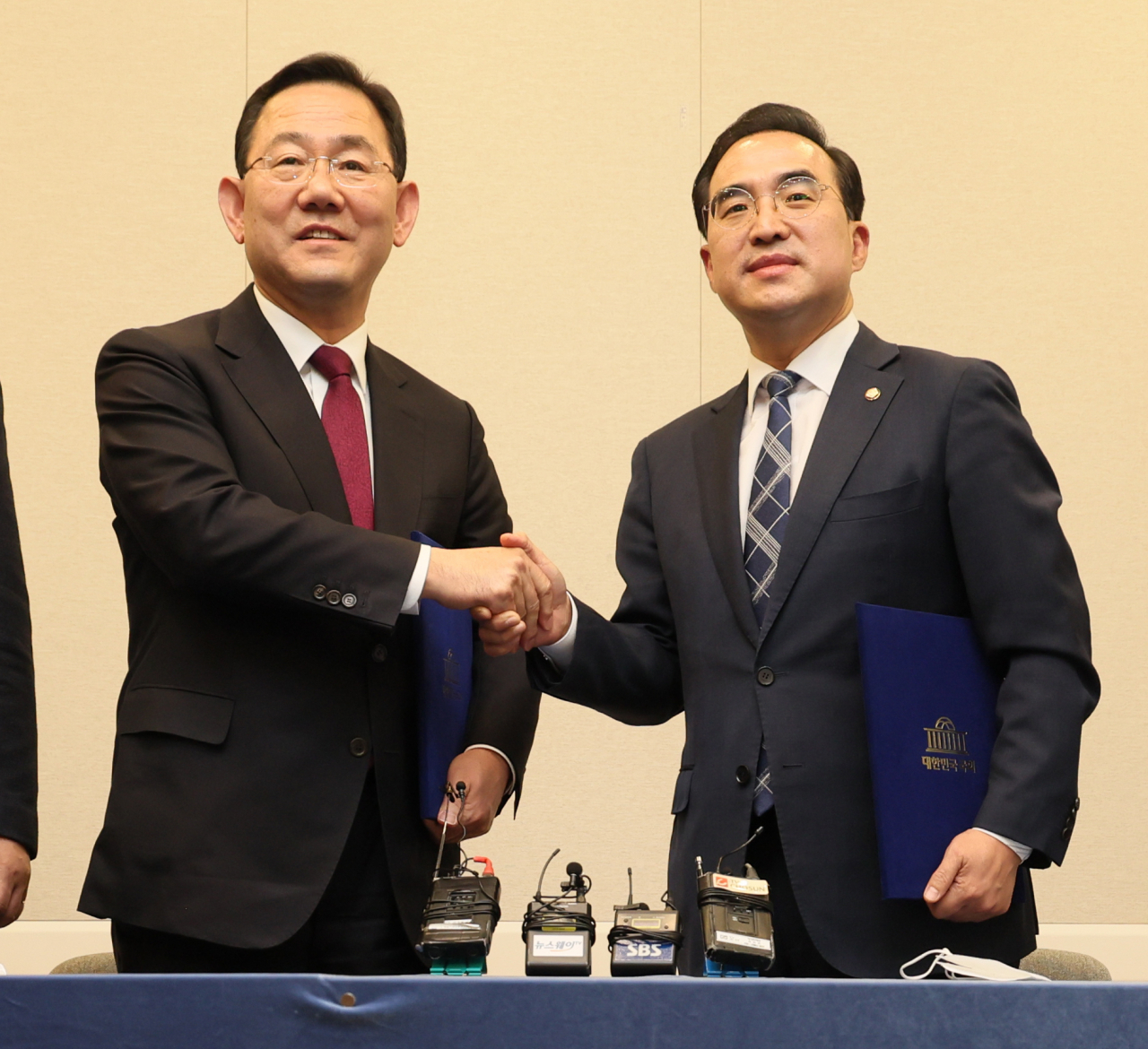 Rep. Joo Ho-young (left), the floor leader of the ruling People Power Party, and his main opposition Democratic Party counterpart Rep. Park Hong-keun shake hands after announcing the content of their agreement on a parliamentary probe into the Itaewon tragedy during a press conference held at the National Assembly in Seoul, Wednesday. (Yonhap)