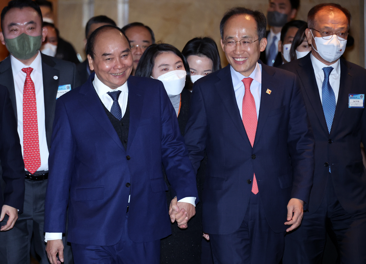 Vietnamese President Nguyen Xuan Phuc (left) and South Korean Finance Minister Choo Kyung-ho hold hands while attending the Korea-Vietnam Business Forum held at Lotte Hotel Seoul, Tuesday. (KCCI)