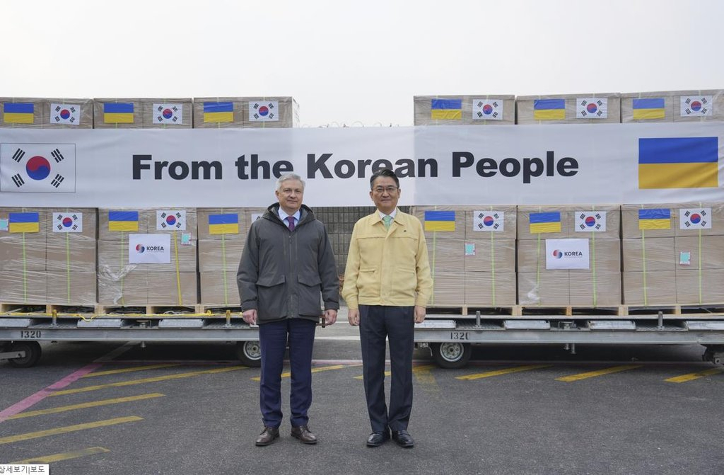Park Yong-min (right), South Korean deputy foreign minister for multilateral and global affairs, and Ukrainian Ambassador to South Korea Dmytro Ponomarenko pose for photos in front of humanitarian aid items prepared to be flown to Ukraine at Incheon International Airport on Friday. (Yonhap)