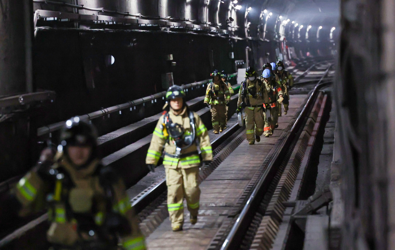 Firefighters walks along a tunnel between Muakjae Station and Dongnimmun Station on Friday. (Yonhap)